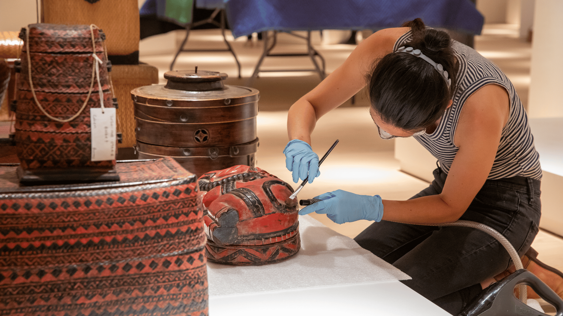 Person using a brush to clean up a art piece on display at Mingei