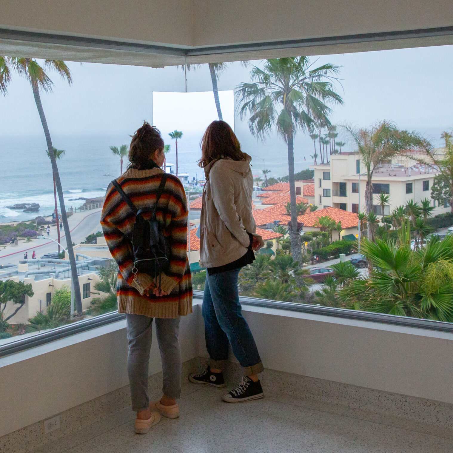 Two museum visitors standing and looking out a window that overlooks La Jolla and the Pacific Ocean.