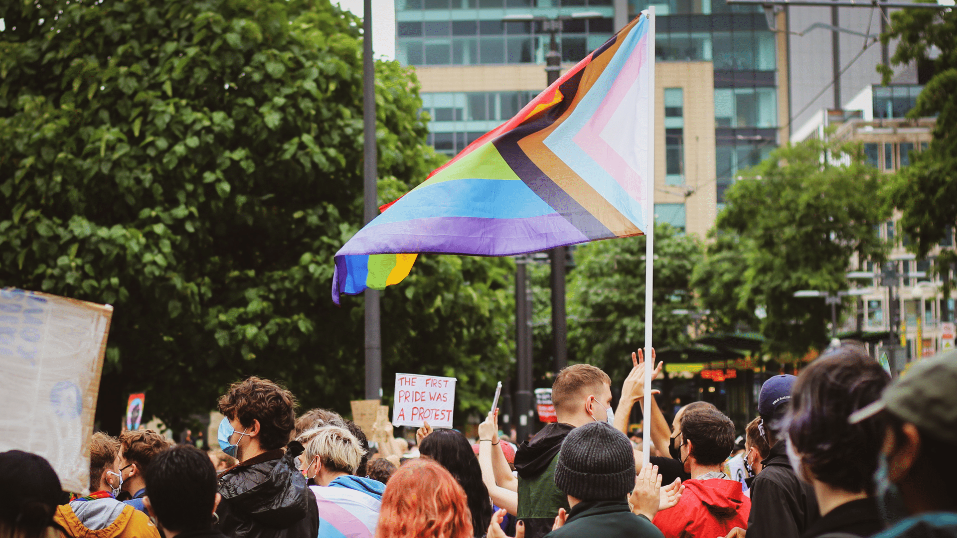 Progressive Pride flag being held up at a street gathering