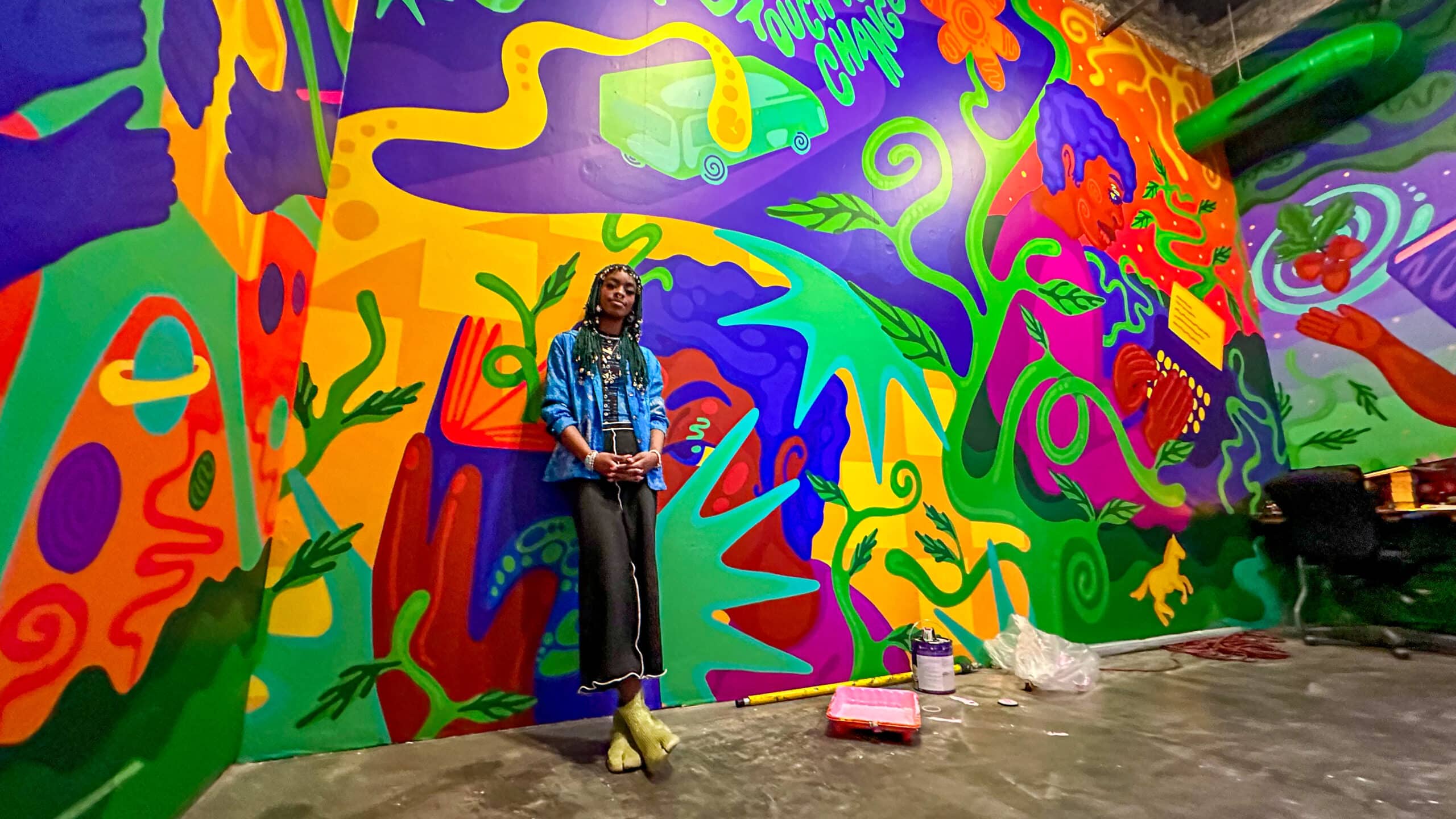 Young artist standing beside colorful mural (photo credit: The New Children's Museum)