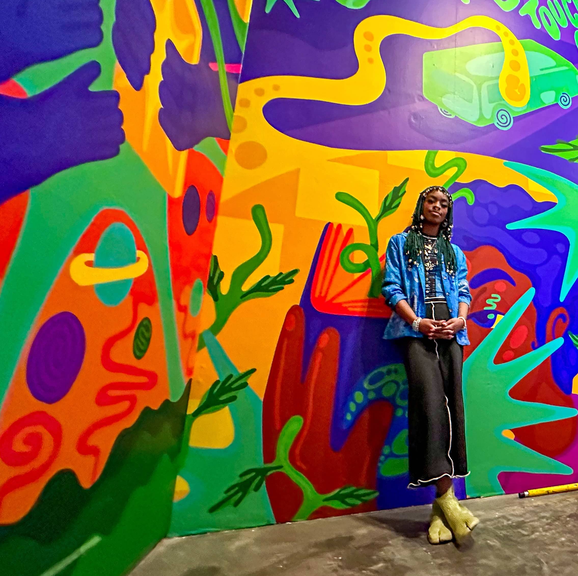 Young artist standing beside colorful mural (photo credit: The New Children's Museum)