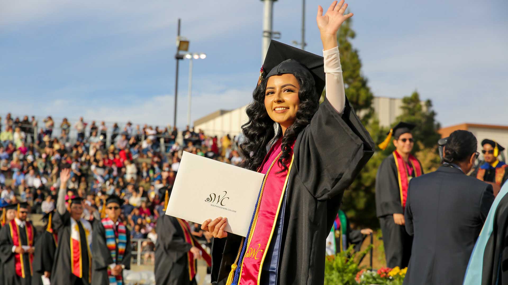 Southwestern College student at graduation holding diploma and waving