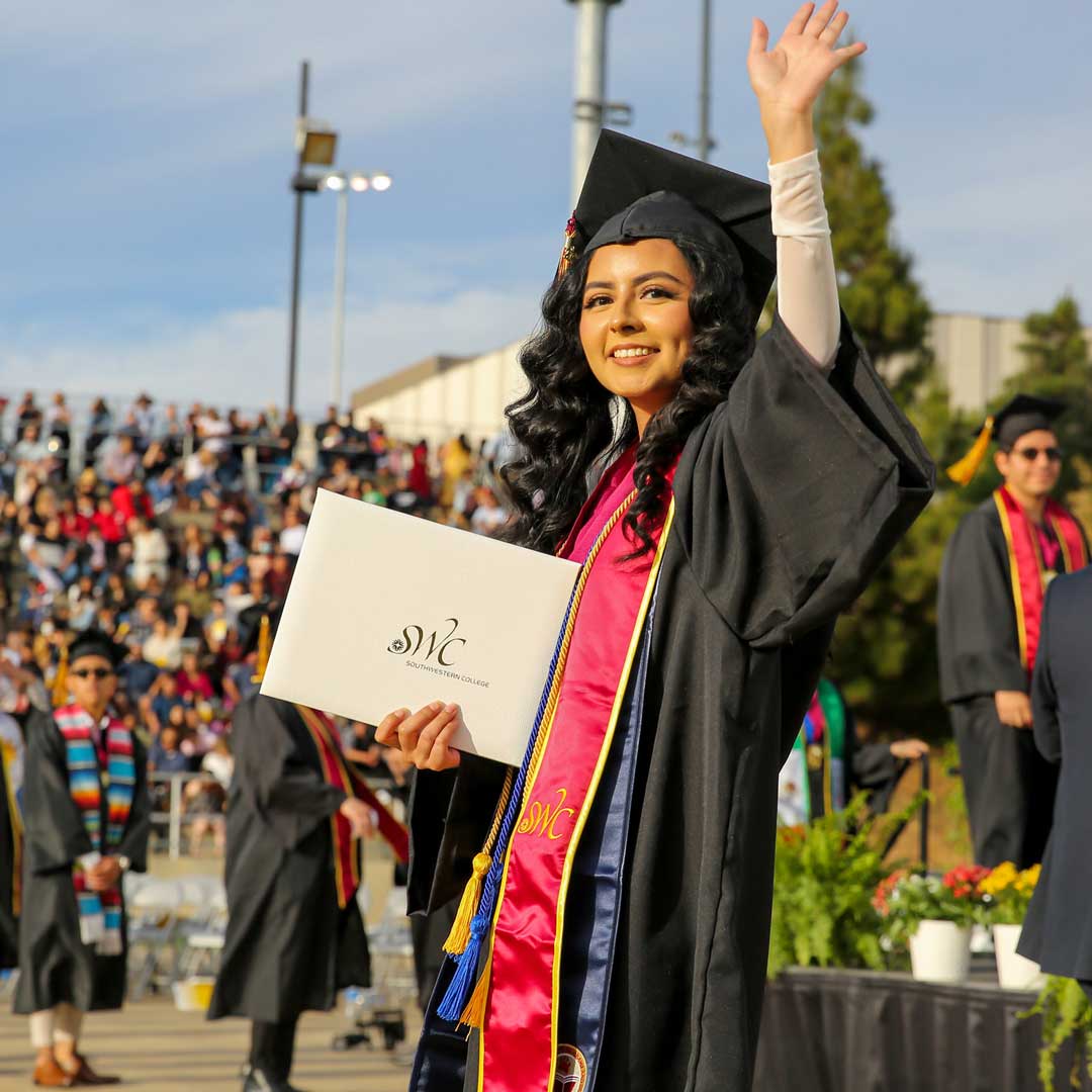 Southwestern College student at graduation holding diploma and waving