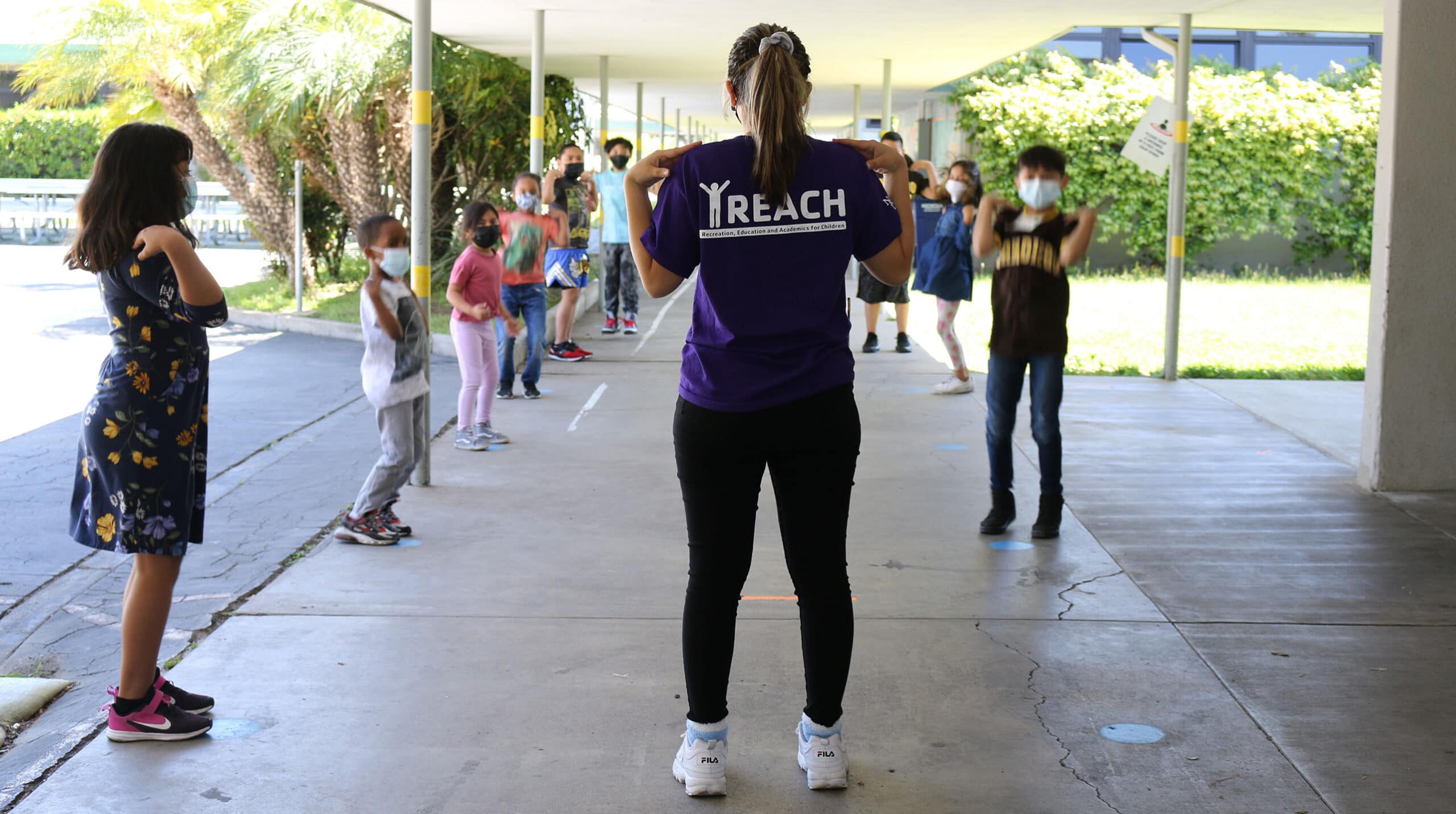 Woman wearing "Y Reach" tee leading activity outside with children