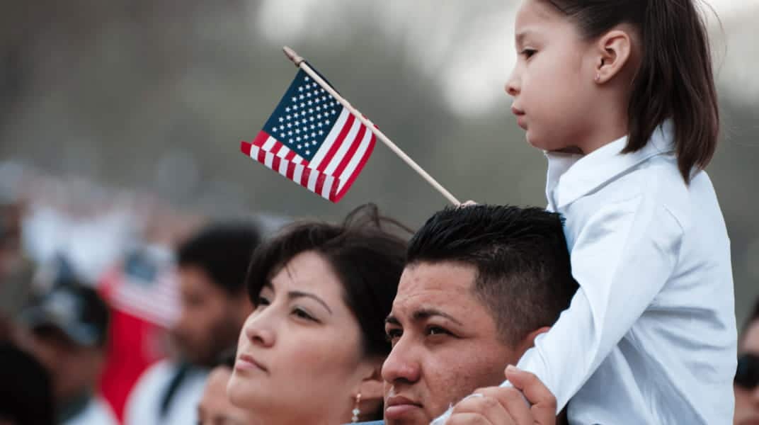 Child sitting on parent's shoulder holding American flag